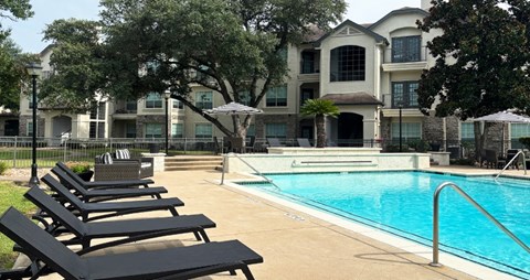 Luxury resort-style swimming pool with fountain, poolside lounges chairs, beautiful landscaping, lush landscaping and scenic views at Village on the Parkway Apartments.