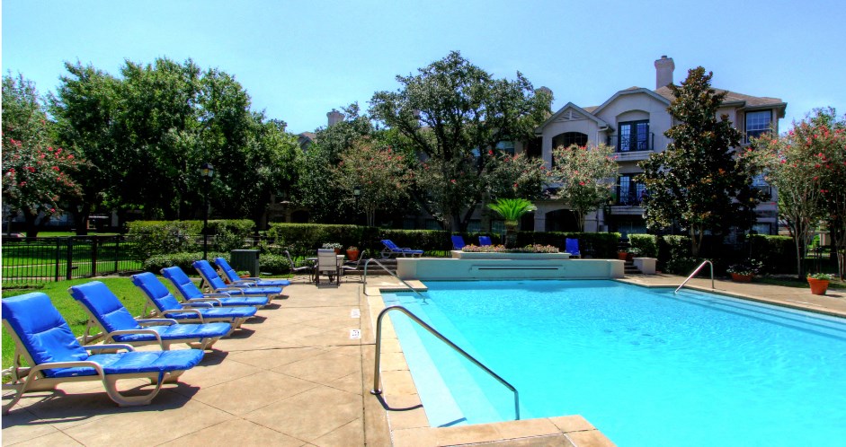 Luxury resort-style swimming pool with fountain, poolside lounges chairs, beautiful landscaping, lush landscaping and scenic views at Village on the Parkway Apartments.