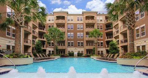 Luxury apartments with resort-style pool, palm trees, spacious sundeck with poolside lounge chairs, grilling station, fountains, and fitness center at Villa Piana Apartments in Dallas