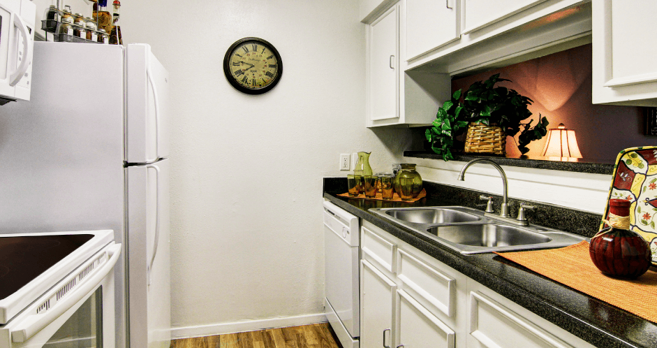 Bright white kitchens with black countertops and wood plank floors at Waters of Winrock Apartments in Houston