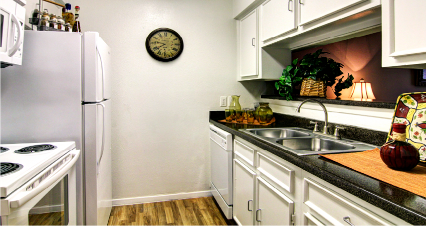 Bright white kitchens with black countertops and wood plank floors at Waters of Winrock Apartments in Houston.