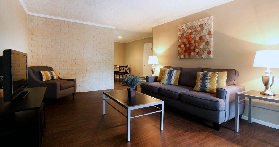 Spacious one and two bedroom floor plans with white brick accent walls and wood plank floors at Waters of Winrock Apartments in Houston.