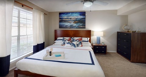A bedroom with a large bed, a ceiling fan, and a painting on the wall.