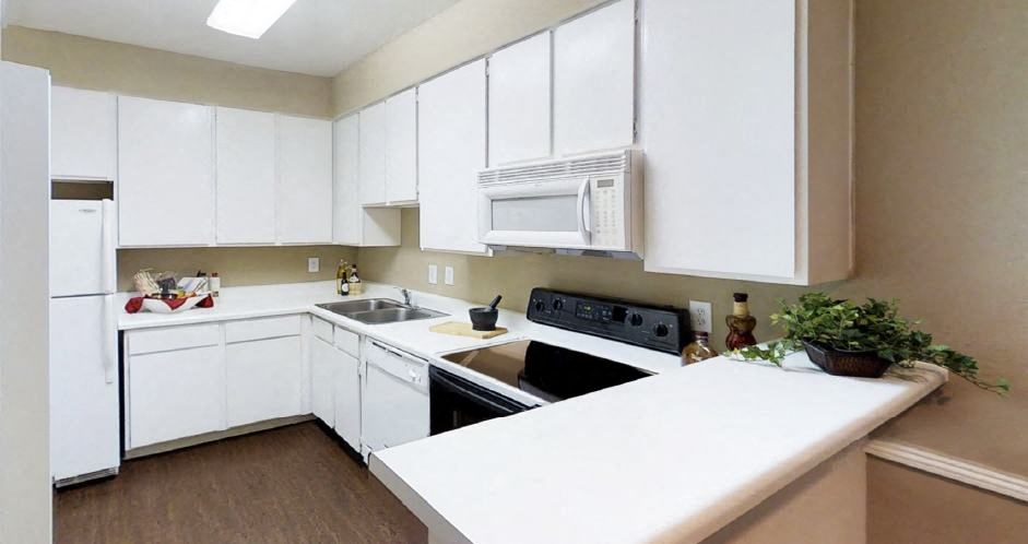 Bright spacious kitchen with white cabinets, breakfast bar, and wood pattern flooring at Woodlake Oaks Apartments in Houston
