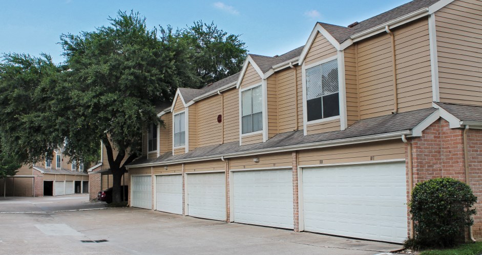 Gated apartment community in the Bayou area of Houston with attached garages, covered parking, 2 swimming pools, lush landscaping, and scenic views at Woodlake Oaks Apartments in Houston.