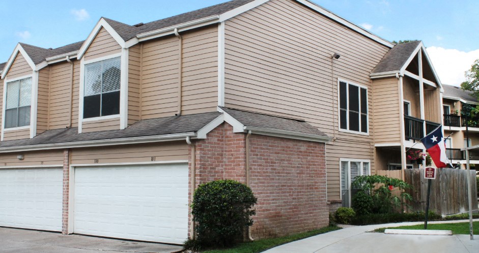 Gated apartment community in the Bayou area of Houston with attached garages, covered parking, 2 swimming pools, lush landscaping, and scenic views at Woodlake Oaks Apartments in Houston.