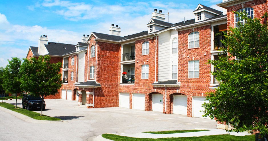 Luxury apartments with red brick exterior, attached garages, lush landscaping, and scenic views at Lenox Village Apartments in Lincoln, Nebraska