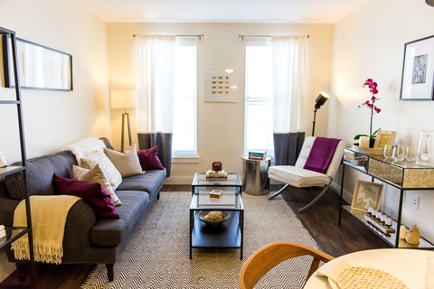 A living room with a grey couch, a coffee table, a chair, and a table with a vase of flowers.