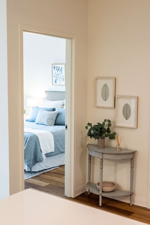 A bedroom with a bed and a table with a plant on it.