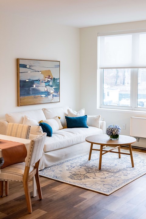 A living room with a white couch, a brown chair, and a painting on the wall.