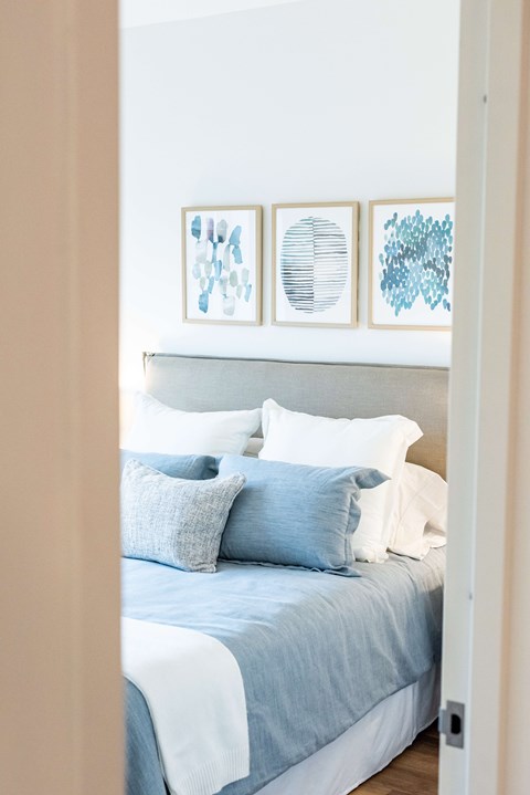 A bed with a blue comforter and pillows is seen from the side.