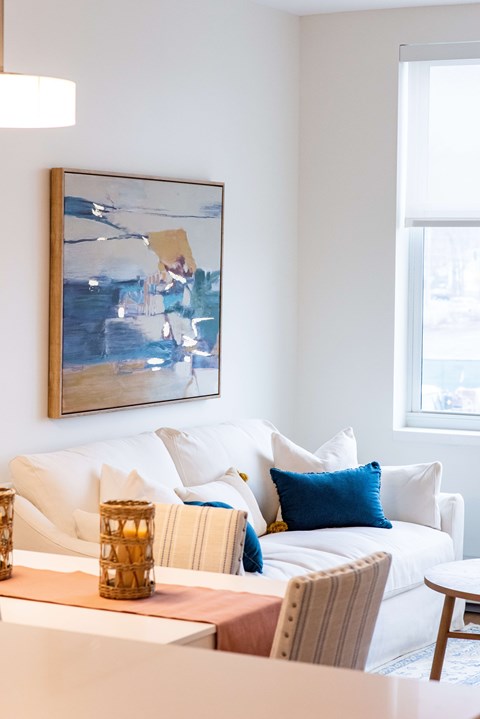 A living room with a white couch and a painting on the wall.