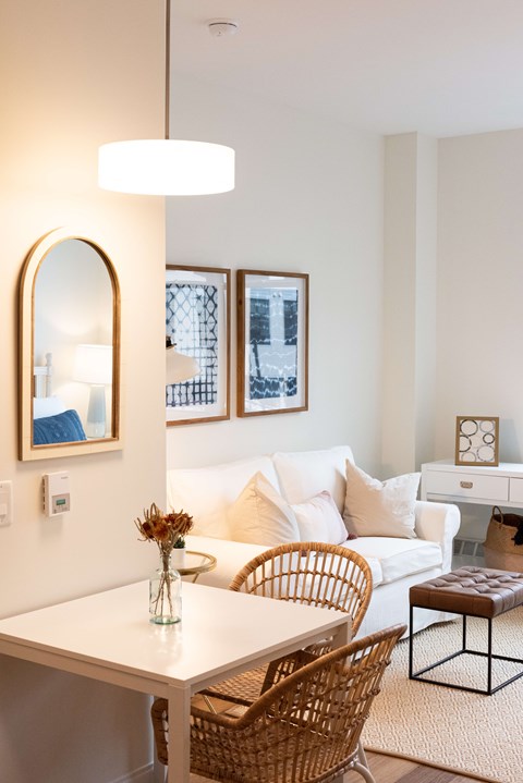 A white dining table with a wicker chair and a brown leather ottoman.