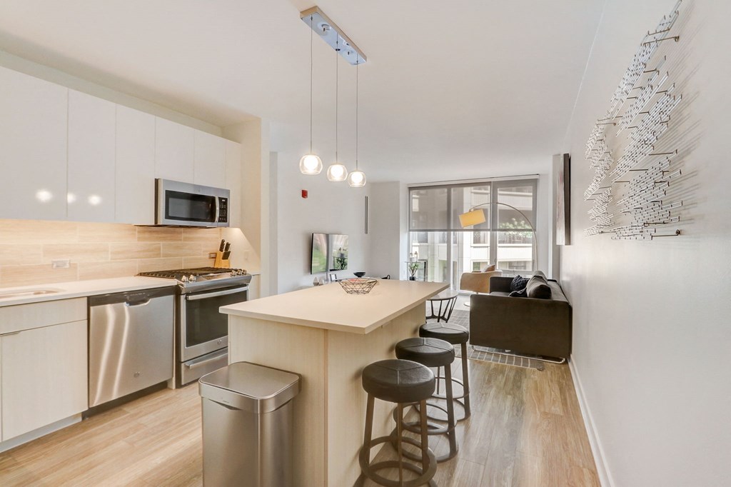 Kitchen with an island and stools next to a living room with a couch and a at The Apartments at Lincoln Common, Chicago