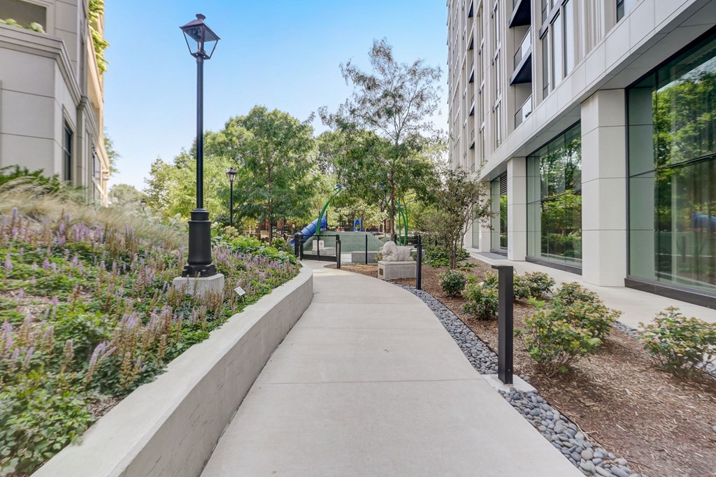 Walkway with a large building on the left and a playground on the right at The Apartments at Lincoln Common, Chicago, IL, 60614