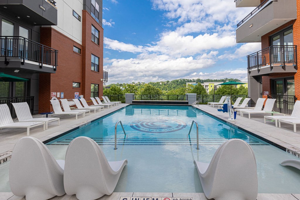 a swimming pool with white chairs at a hotel with a view of the city