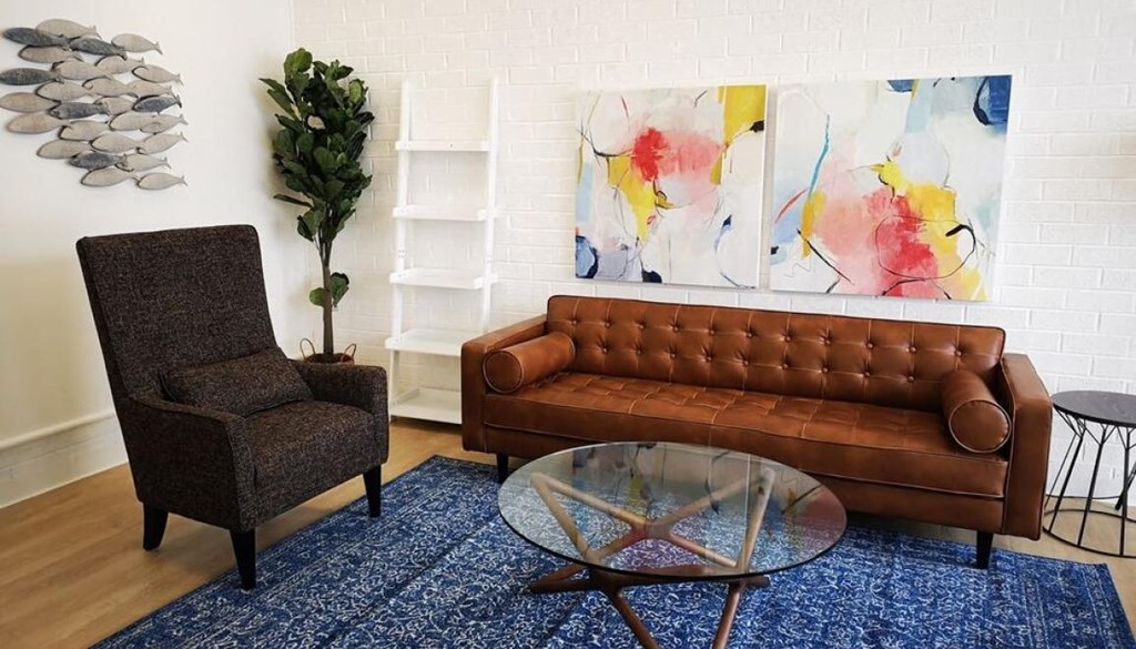 A brown leather couch sits in front of a painting in a living room.