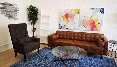 A brown leather couch sits in front of a painting in a living room.
