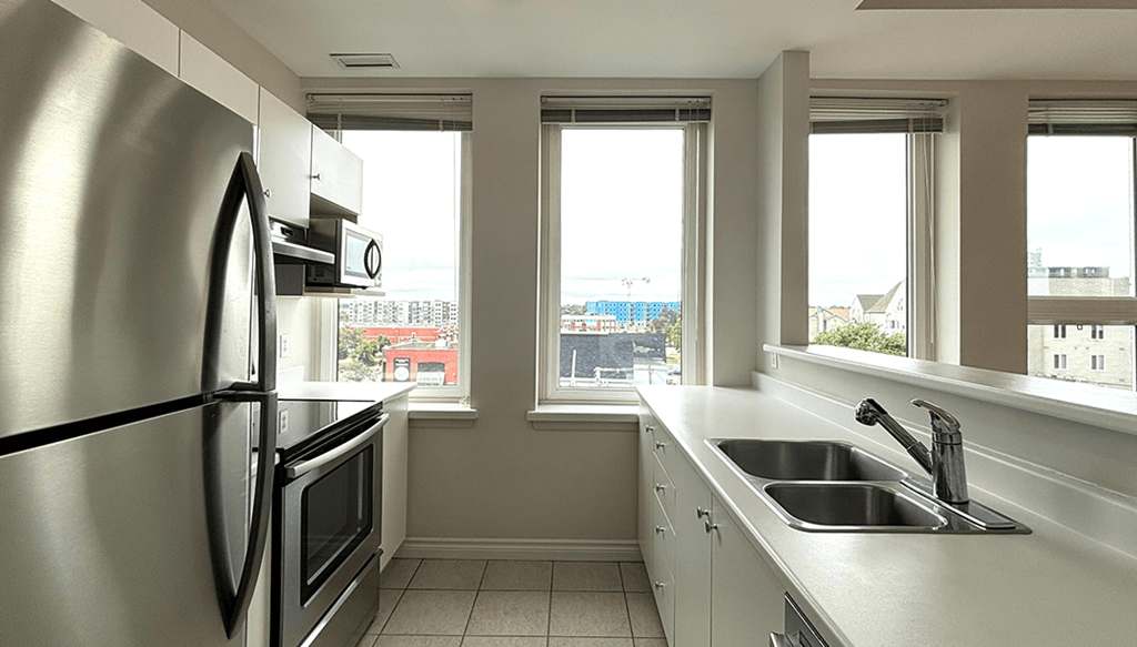 A kitchen with a stainless steel refrigerator and a window overlooking a cityscape.