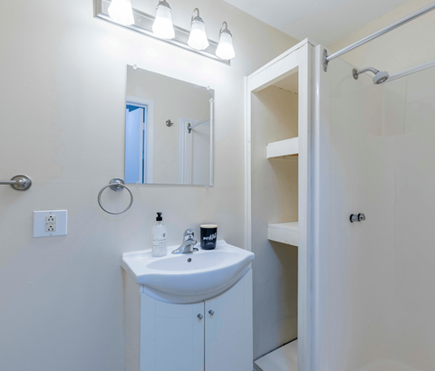 A white bathroom with a sink, mirror, and shower.