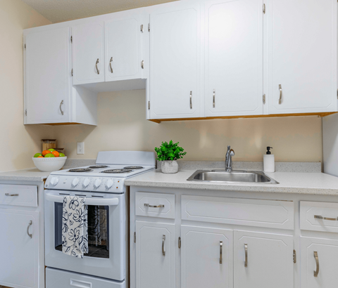 A white kitchen with a stove, sink, and cabinets.