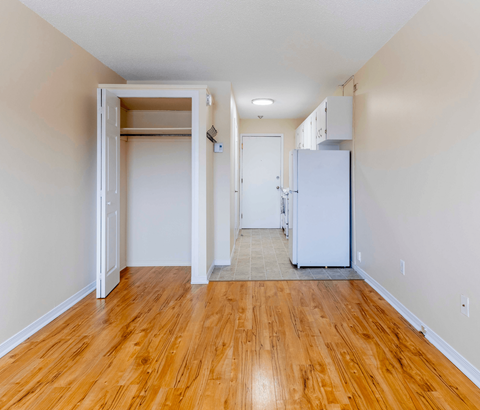 A room with a white fridge and wooden floors.