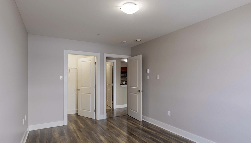 A room with a white ceiling and a wooden floor with three doors.