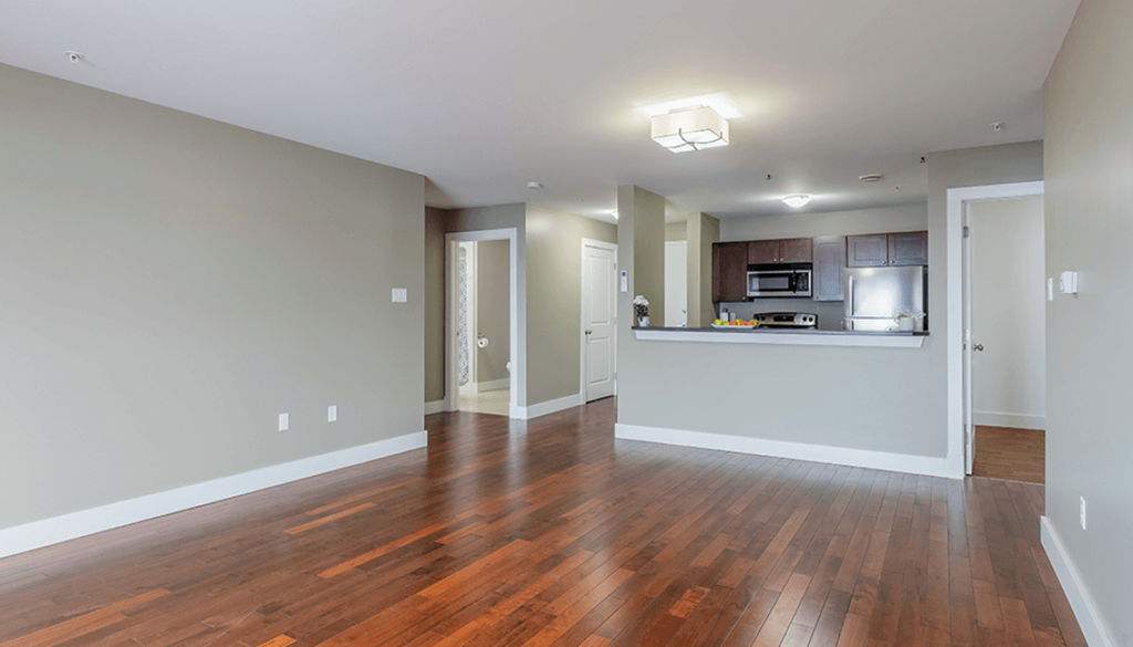 A spacious living room with hardwood floors and a kitchen in the background.