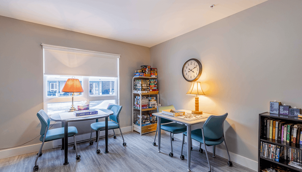 A room with a table, chairs, a clock, and a bookshelf.
