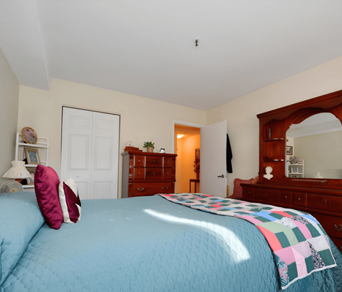 A bedroom with a blue bedspread and a wooden dresser.