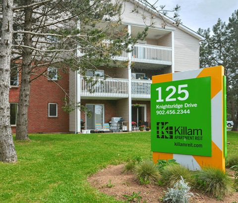 A sign for Killam Apartment Rent in front of a building.