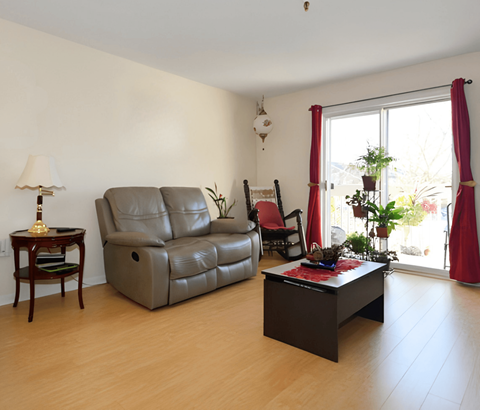 A living room with a grey leather sofa, a wooden side table with a lamp, a red chair, and a black coffee table.