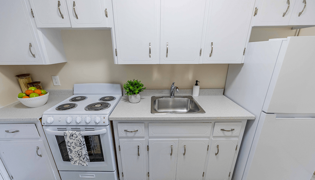 A white kitchen with a stove, sink, and cabinets.