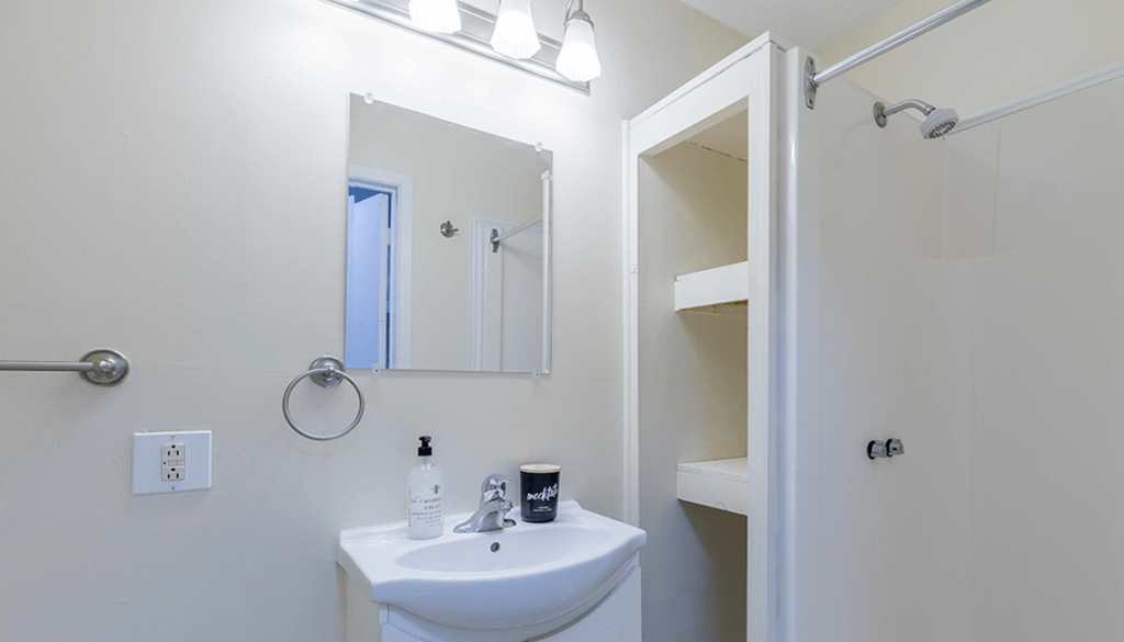 A white sink with a mirror above it and a shower in the background.