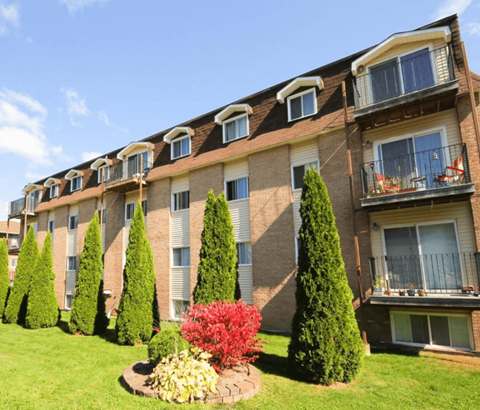 A row of apartment buildings with balconies and trees in front.