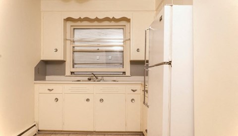 A white kitchen with a refrigerator, sink, and cabinets.