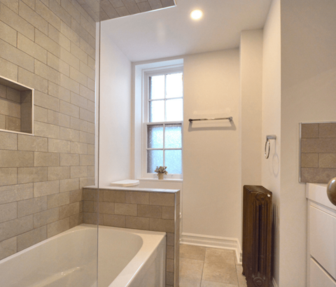 A bathroom with a tub, window, and radiator.