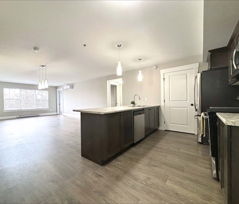 A kitchen with a dark brown island and light wood flooring.