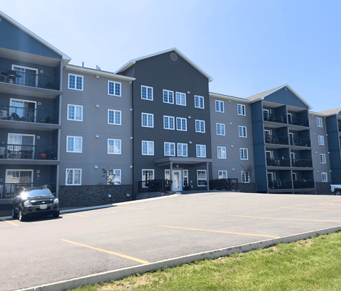A black car is parked in a parking lot in front of a large apartment building.