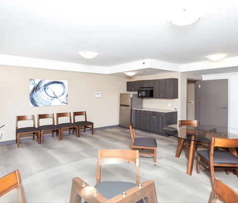 A modern dining room with a large painting on the wall and a kitchen area in the background.