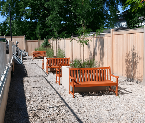 A row of orange benches are lined up on a gravel path.