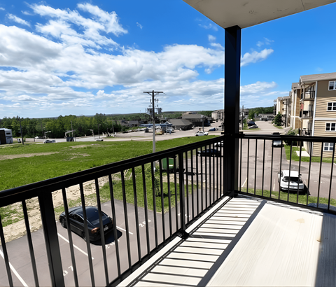 A balcony with a black railing overlooks a parking lot and buildings.