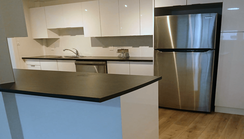 A modern kitchen with a stainless steel refrigerator and a black countertop.