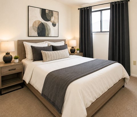 A bedroom with a large bed, a nightstand with a lamp, and a painting on the wall.