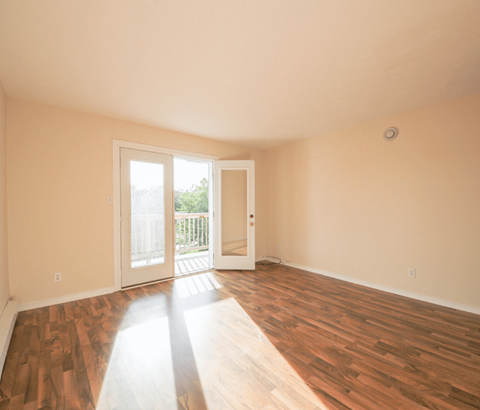 A room with wooden floors and a door leading to a balcony.