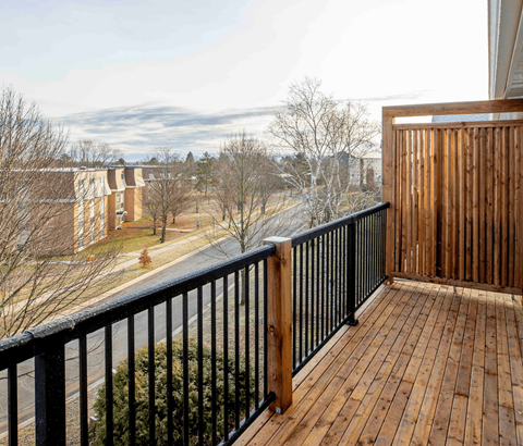 A balcony with a black railing and wooden floor overlooks a residential area.