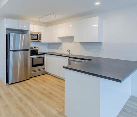 A modern kitchen with a stainless steel refrigerator and wooden flooring.
