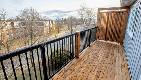 A wooden deck with a black railing and a view of a town in the distance.