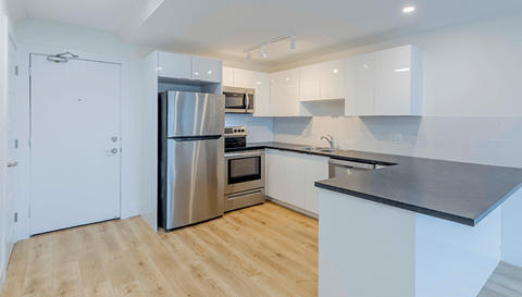 A modern kitchen with a stainless steel refrigerator and wooden flooring.