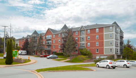 A large red and grey apartment building with cars parked in front.